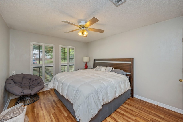 bedroom with a ceiling fan, a textured ceiling, visible vents, wood finished floors, and baseboards