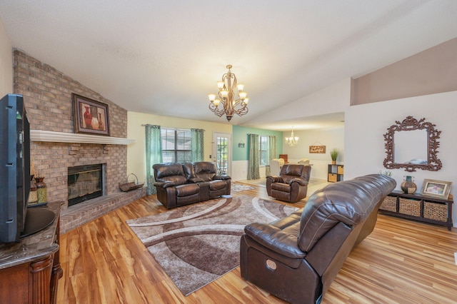 living room featuring an inviting chandelier, vaulted ceiling, wood finished floors, and a brick fireplace