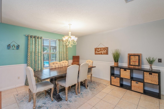 dining space featuring an inviting chandelier, a textured ceiling, light tile patterned floors, and a wainscoted wall
