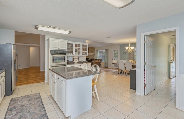kitchen with a kitchen breakfast bar, white cabinets, a chandelier, appliances with stainless steel finishes, and light tile patterned floors