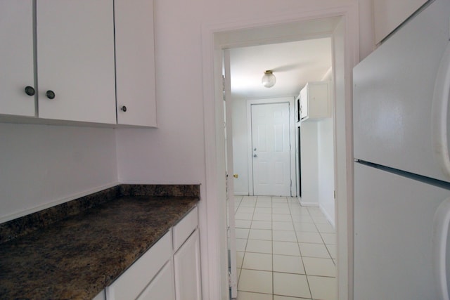 kitchen featuring freestanding refrigerator, white cabinetry, light tile patterned flooring, and dark stone countertops
