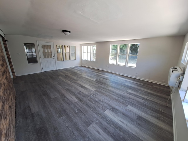unfurnished living room featuring baseboards, a wall mounted air conditioner, dark wood finished floors, and a barn door
