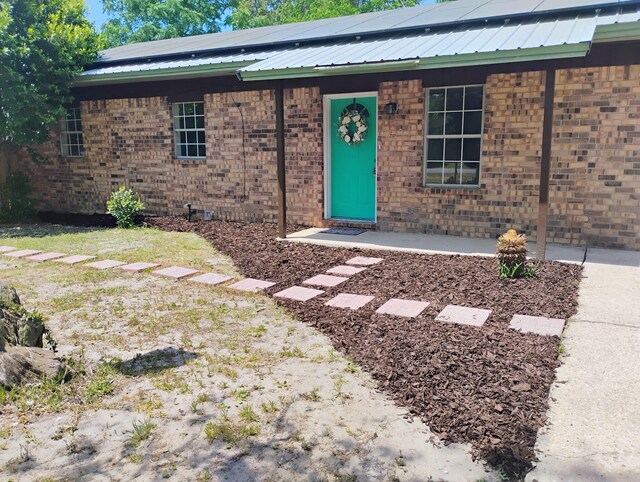 view of front of property featuring roof mounted solar panels, metal roof, and brick siding