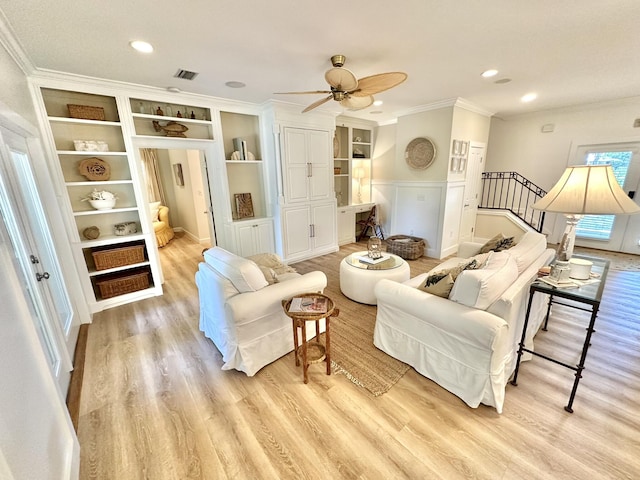 living room featuring ornamental molding, wood finished floors, a wainscoted wall, a ceiling fan, and stairway