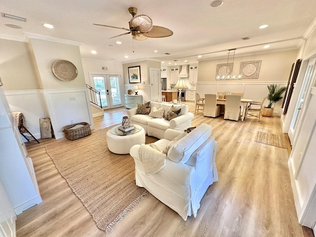 living room featuring crown molding, ceiling fan, light wood-style flooring, a wainscoted wall, and a decorative wall