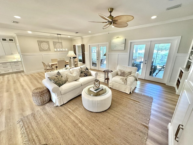 living room with french doors, a decorative wall, plenty of natural light, crown molding, and light wood-style floors
