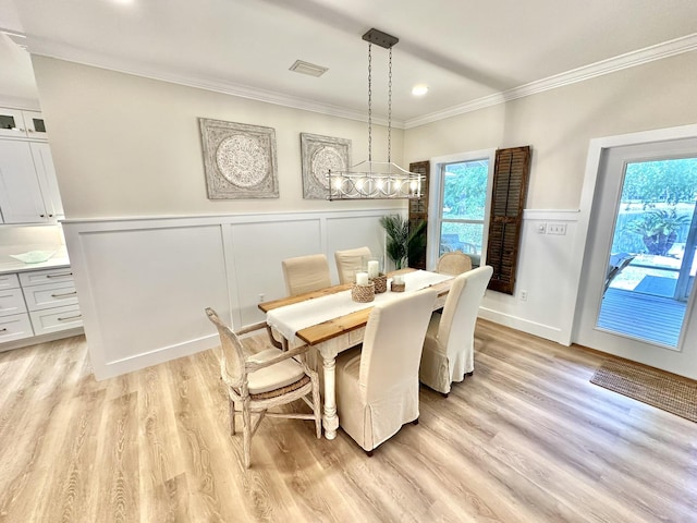 dining area featuring a decorative wall, crown molding, light wood-type flooring, and wainscoting