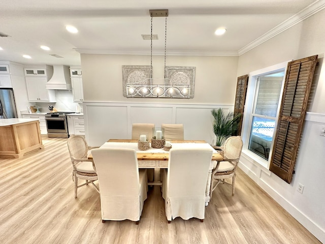 dining room featuring ornamental molding, light wood-style flooring, a decorative wall, wainscoting, and recessed lighting