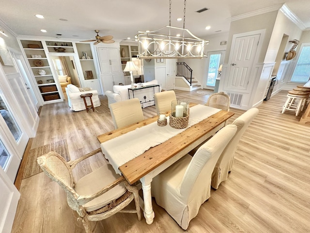 dining room with crown molding, light wood-type flooring, stairway, ceiling fan, and built in shelves
