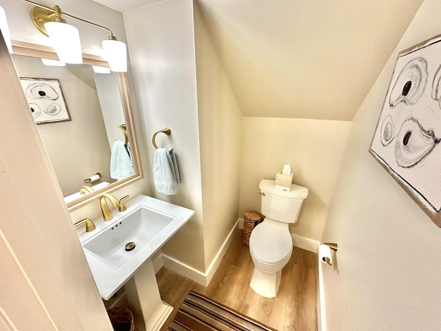 bathroom featuring a sink, wood finished floors, toilet, baseboards, and vaulted ceiling