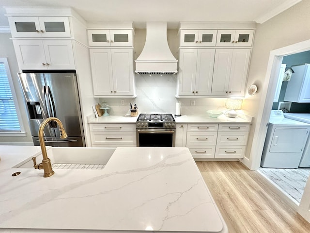 kitchen featuring washing machine and dryer, appliances with stainless steel finishes, premium range hood, light wood-style floors, and white cabinetry