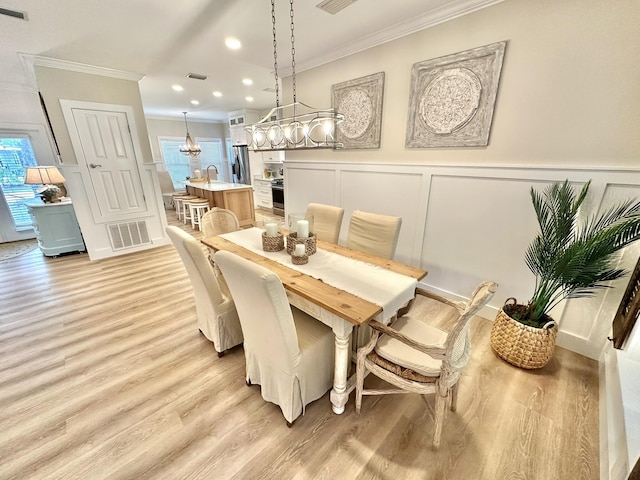 dining room featuring crown molding, a decorative wall, light wood-style floors, recessed lighting, and wainscoting