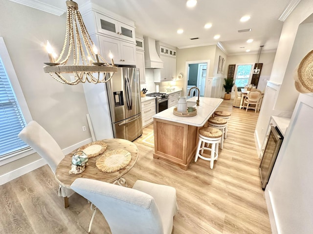 kitchen featuring appliances with stainless steel finishes, premium range hood, ornamental molding, an island with sink, and light countertops