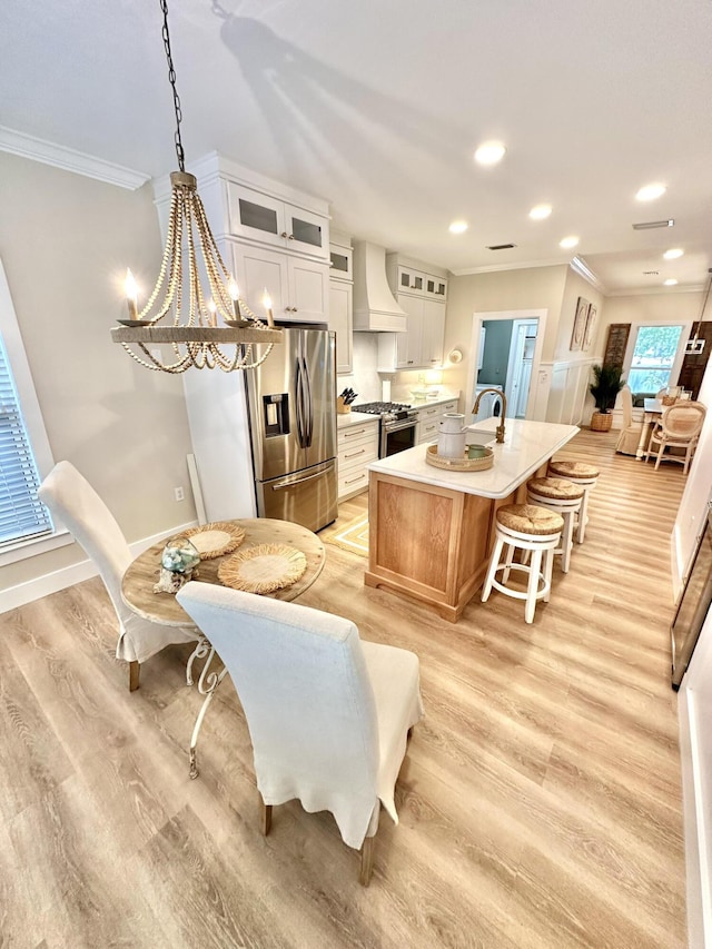 kitchen featuring appliances with stainless steel finishes, custom range hood, ornamental molding, light wood-style flooring, and a chandelier