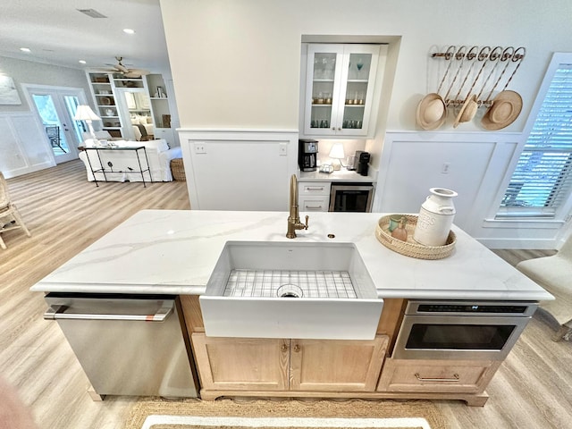 kitchen with a sink, light wood-type flooring, stainless steel dishwasher, wine cooler, and glass insert cabinets