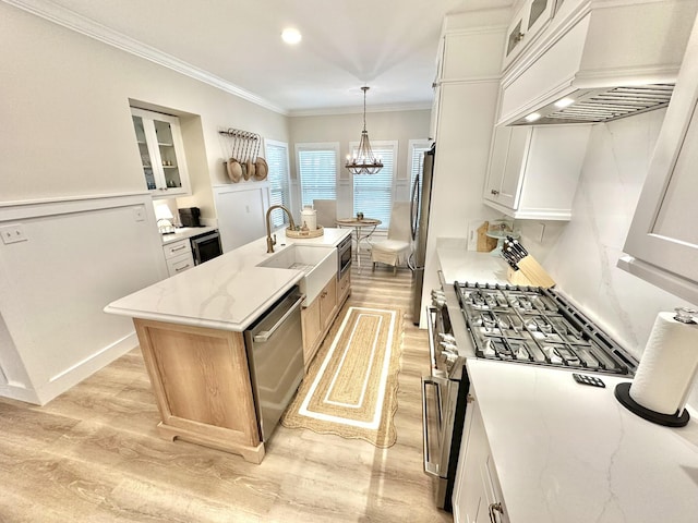 kitchen with appliances with stainless steel finishes, custom exhaust hood, light wood finished floors, a center island with sink, and glass insert cabinets
