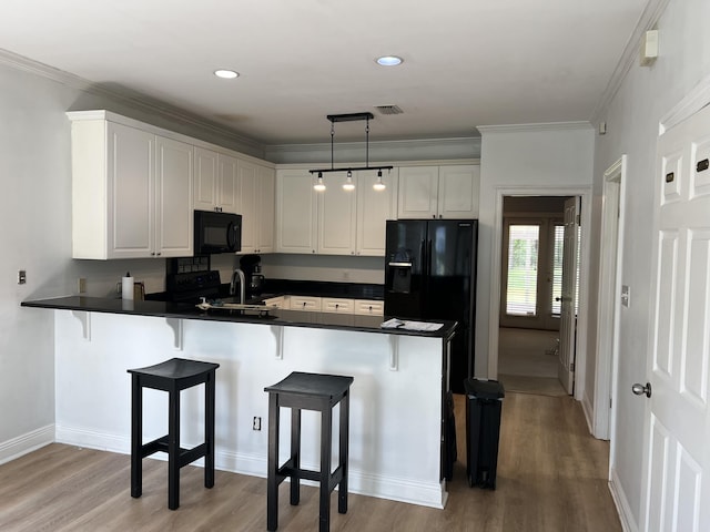 kitchen featuring a peninsula, black appliances, dark countertops, and a kitchen breakfast bar