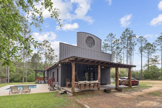 rear view of property featuring a lawn, board and batten siding, an outdoor pool, and a wooden deck