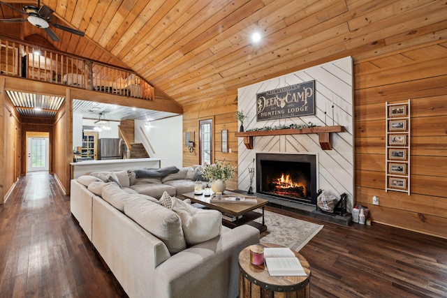 living area featuring dark wood-style flooring, wood walls, a large fireplace, a ceiling fan, and vaulted ceiling