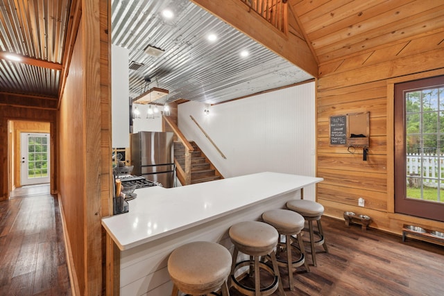 bar with dark wood-type flooring, freestanding refrigerator, wooden walls, and stairway