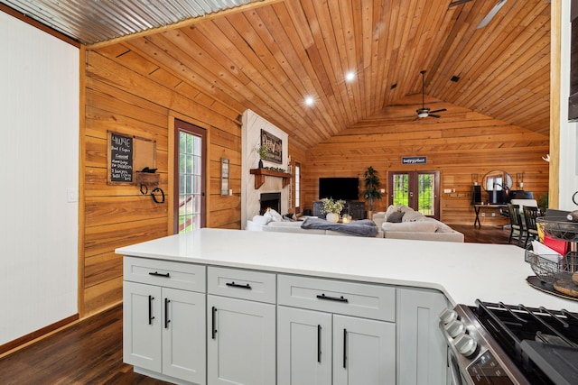 kitchen featuring wooden walls, ceiling fan, stainless steel range with gas cooktop, open floor plan, and vaulted ceiling