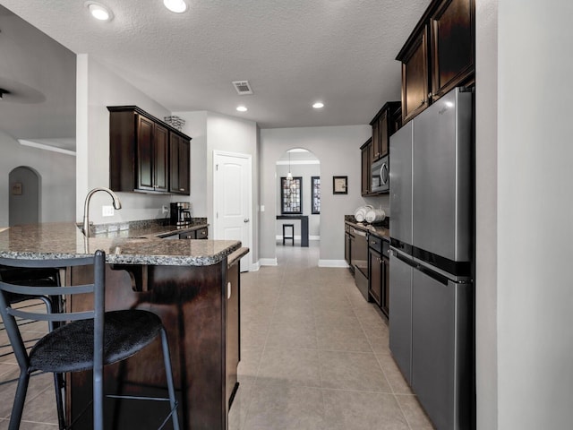 214 Whispering Lake Dr, Santa Rosa Beach, FL 32459 - kitchen with a sink, a peninsula, stainless steel appliances, dark brown cabinetry, and arched walkways
