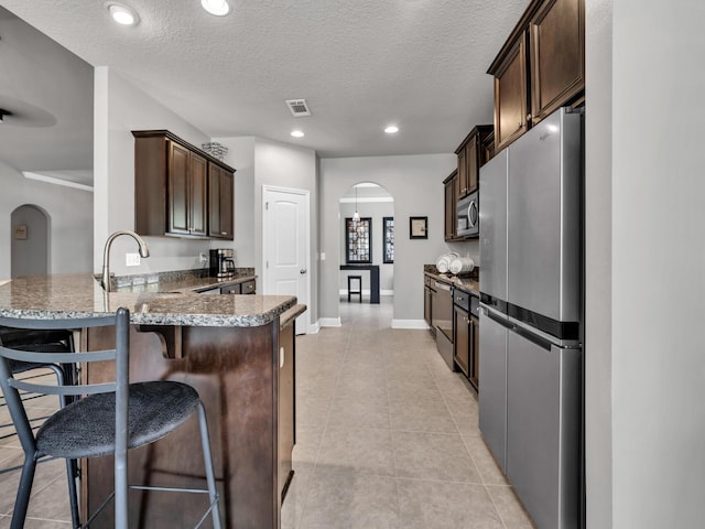 214 Whispering Lake Dr, Santa Rosa Beach, FL 32459 - kitchen with appliances with stainless steel finishes, arched walkways, a sink, dark brown cabinetry, and a textured ceiling