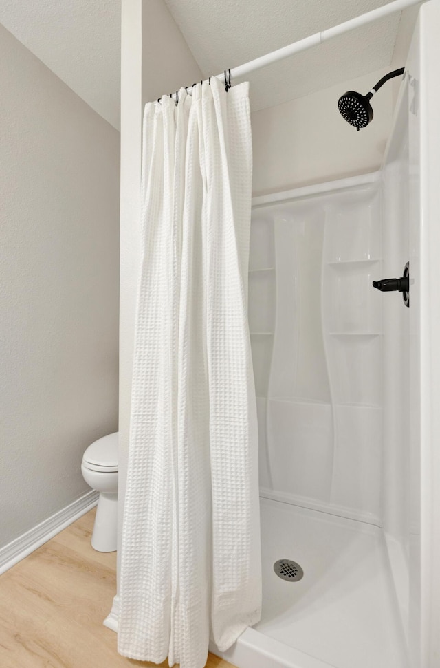 bathroom featuring wood finished floors, baseboards, a stall shower, and toilet