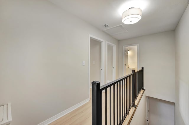 corridor with baseboards, visible vents, light wood-style flooring, and an upstairs landing