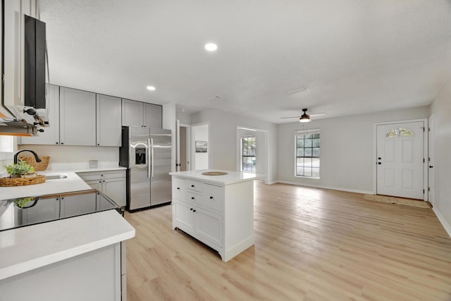 kitchen featuring ceiling fan, a sink, light countertops, light wood-type flooring, and stainless steel refrigerator with ice dispenser