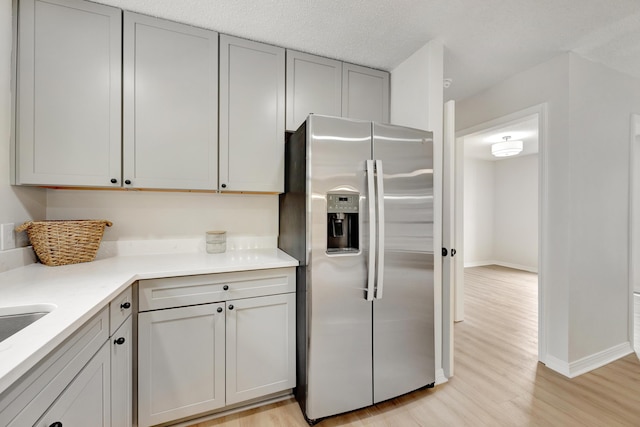 kitchen with light countertops, baseboards, gray cabinetry, light wood finished floors, and stainless steel fridge