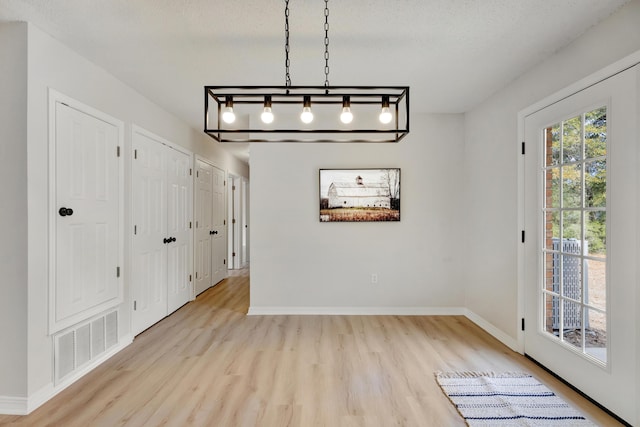 unfurnished dining area with baseboards, light wood finished floors, and visible vents