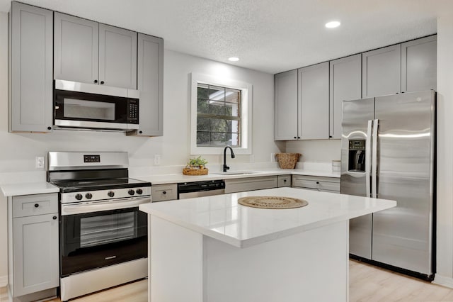 kitchen featuring a sink, light wood finished floors, gray cabinets, a center island, and stainless steel appliances