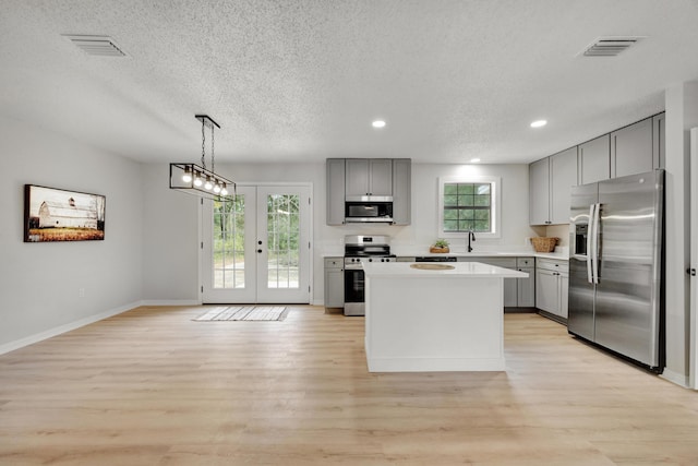 kitchen featuring a kitchen island, gray cabinetry, light countertops, a sink, and stainless steel appliances