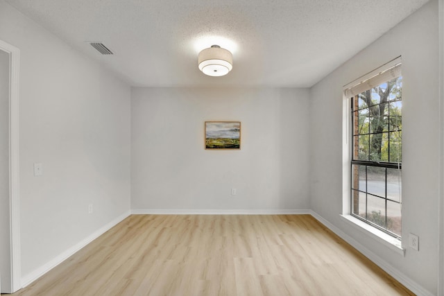 empty room with a textured ceiling, visible vents, baseboards, and light wood-type flooring