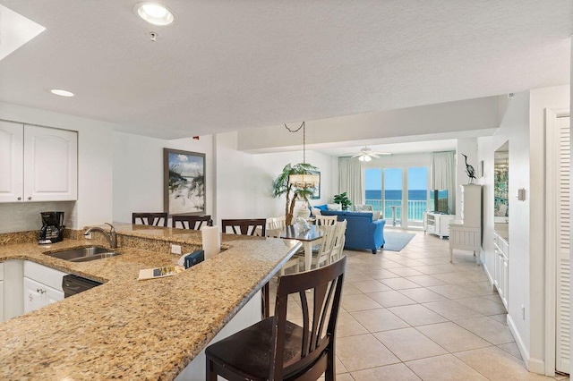 kitchen featuring a sink, a kitchen breakfast bar, recessed lighting, white cabinetry, and light stone countertops