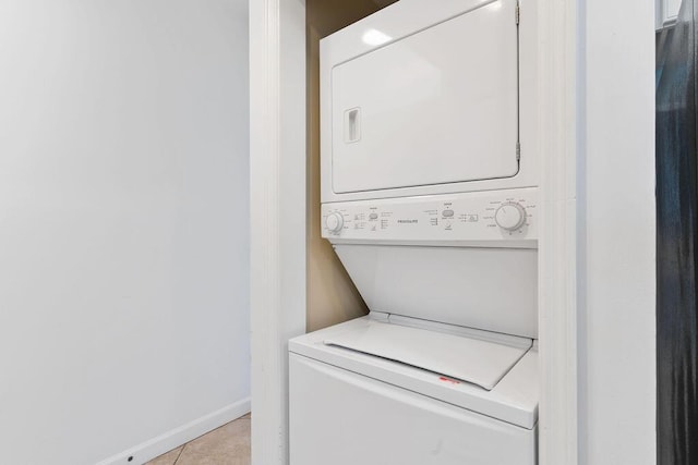 laundry area featuring stacked washer / drying machine, tile patterned flooring, and baseboards