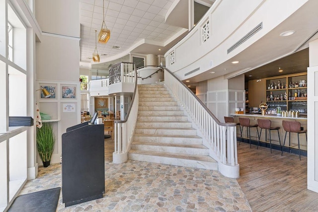 stairs featuring a community bar, a towering ceiling, recessed lighting, and wood finished floors