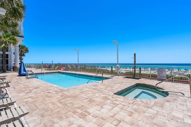 community pool with a community hot tub, fence, a patio, and a water view