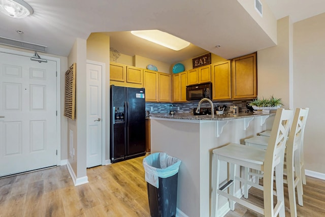 kitchen with a kitchen bar, visible vents, black appliances, light wood finished floors, and dark stone countertops
