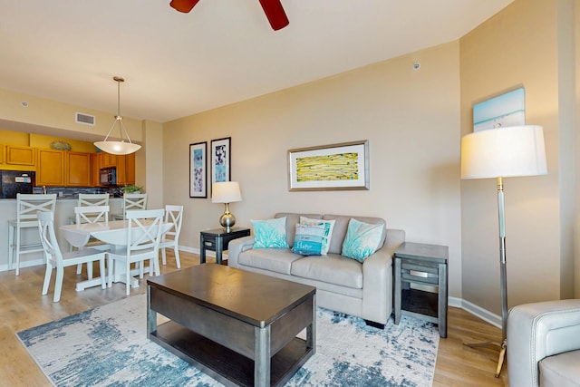 living area featuring baseboards, a ceiling fan, light wood-type flooring, and visible vents