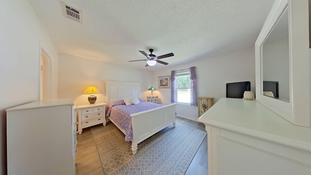 bedroom with visible vents, a textured ceiling, light wood-style flooring, and ceiling fan
