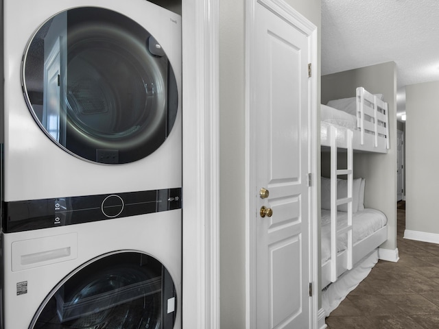 clothes washing area with baseboards, stacked washer / drying machine, a textured ceiling, and laundry area