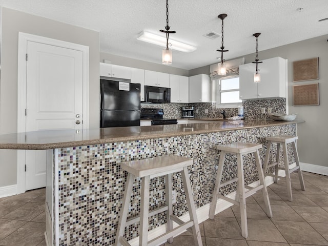 kitchen with white cabinets, a breakfast bar area, baseboards, visible vents, and black appliances