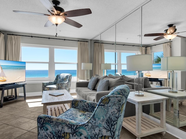tiled living area featuring a ceiling fan, a textured ceiling, baseboards, and a water view