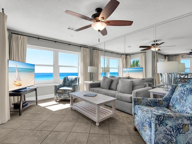 living area featuring a ceiling fan, a textured ceiling, visible vents, and tile patterned flooring
