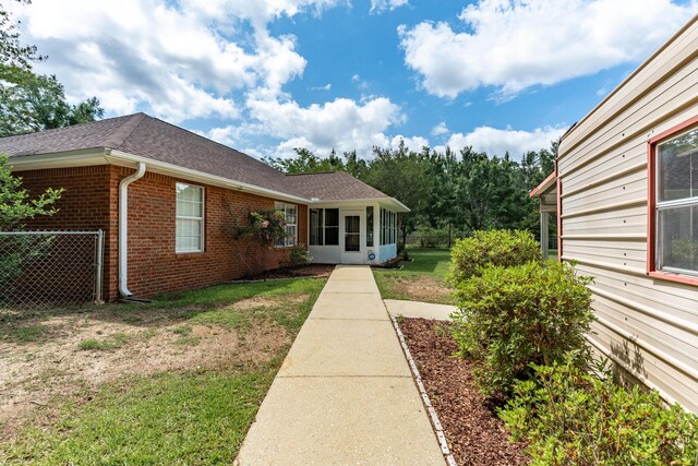 6100 Buck Ward Rd, Baker, FL 32531 - view of home's exterior featuring fence, brick siding, a shingled roof, a sunroom, and a lawn