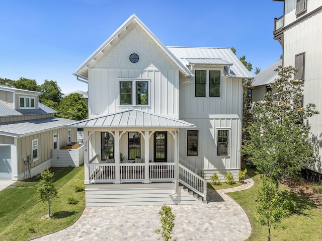 modern inspired farmhouse featuring covered porch, a front yard, metal roof, board and batten siding, and a standing seam roof
