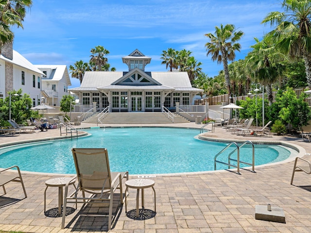 community pool with a patio area, stairs, and fence