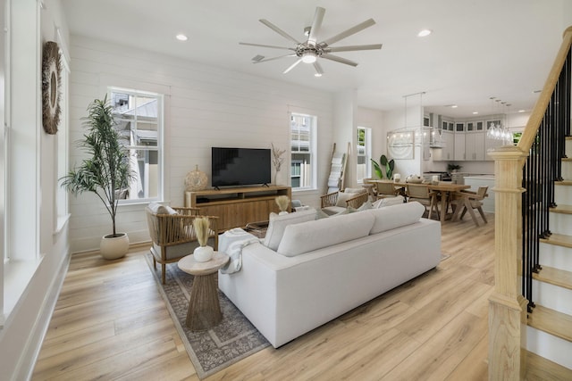 living area with stairs, light wood finished floors, recessed lighting, and ceiling fan with notable chandelier